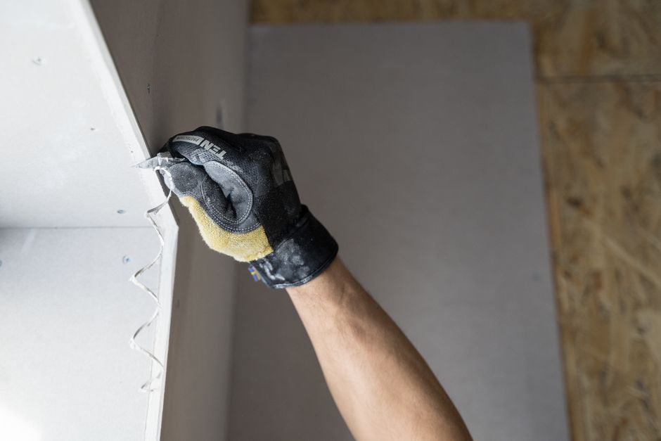 Close-up of a gloved hand applying plaster to an interior wall.
