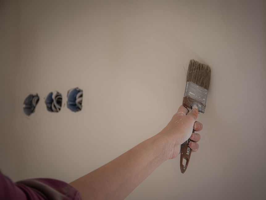 A person painting a wall with a brush, showcasing a home makeover process.